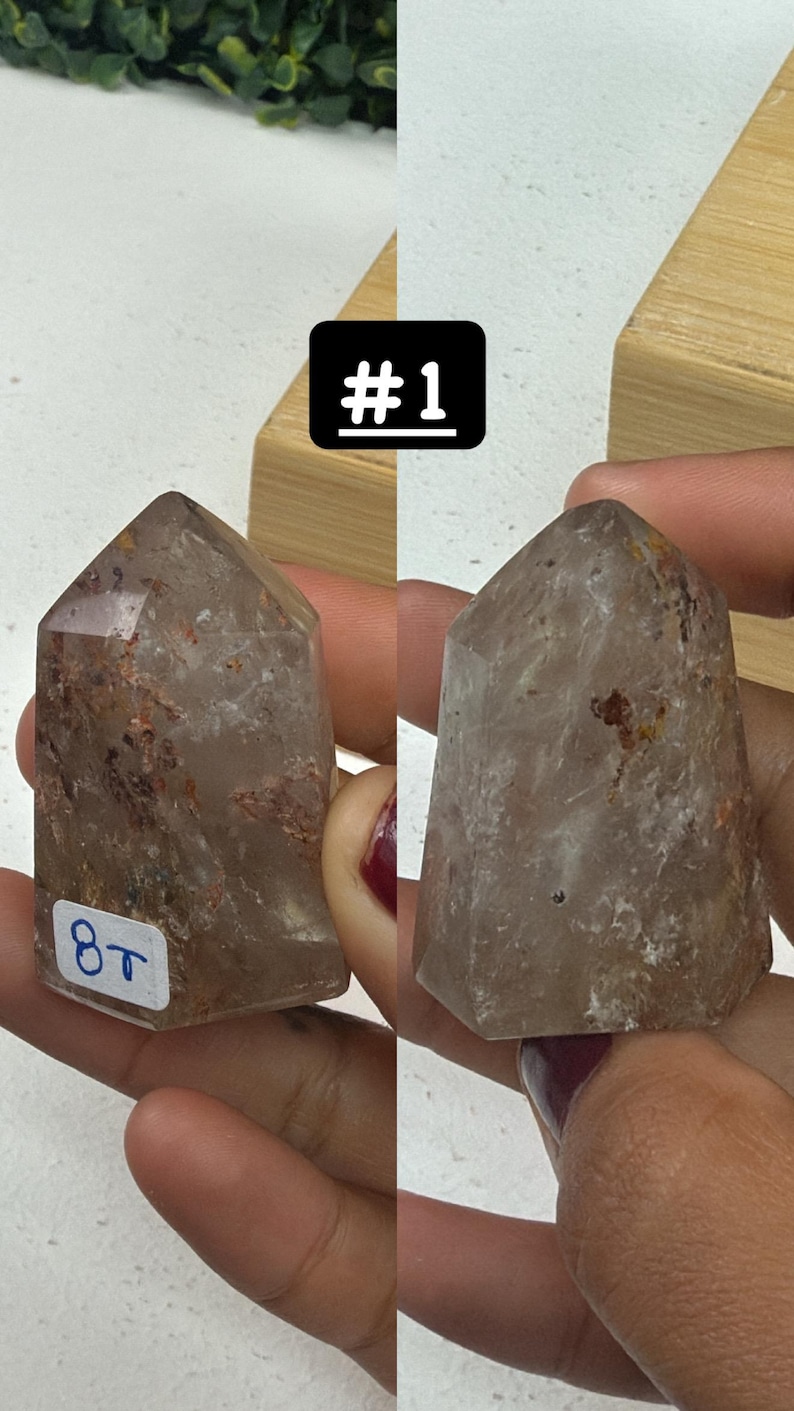 May include: Two clear quartz crystal points with inclusions, one labeled "#1" and the other with "8T". The crystals are held in a person's hands. The crystals have a pointed top and a faceted body.