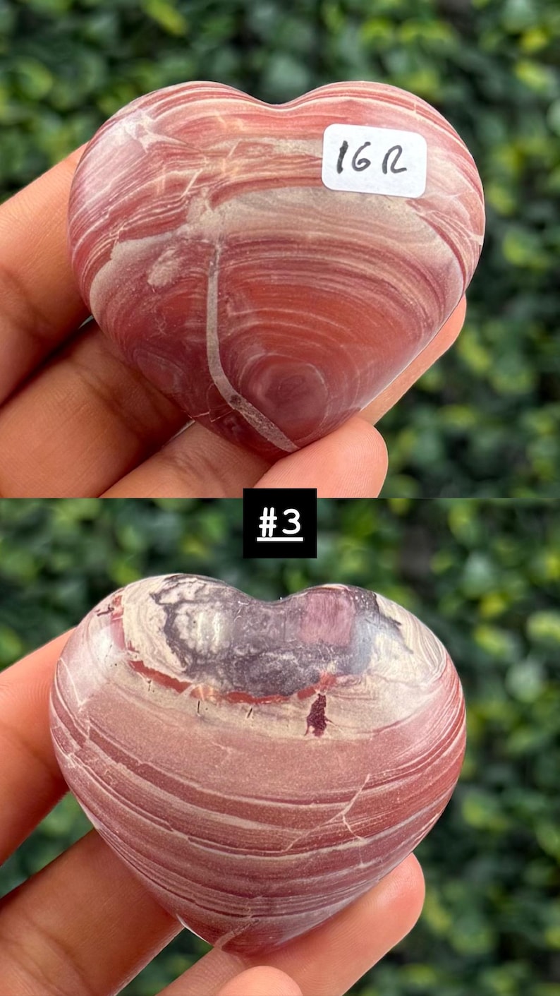 May include: Two heart-shaped stones with a swirling pattern of red, white, and purple hues. One stone has a sticker that reads "16 R", and the other has a sticker that reads "#3". The stones are held in a hand.