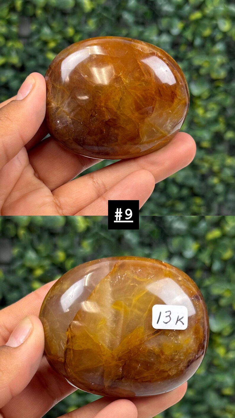 May include: A polished, oval-shaped gemstone with a warm, amber color and internal golden inclusions. The stone is held in a hand against a blurred green background. The text "#9" and "13K" are visible.
