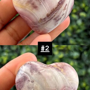 May include: A heart-shaped stone with a mix of purple, white, and brown hues. The stone has a smooth, polished surface. A small white sticker with the text "13K" is attached to the stone. The image also includes the text "#2".