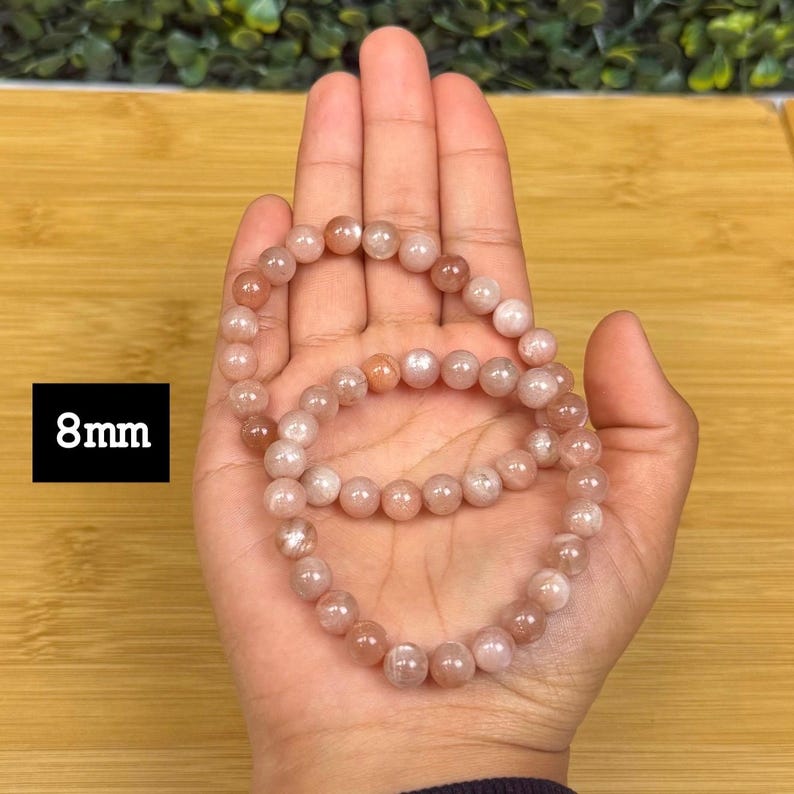 Op de afbeelding: Twee armbanden van perzik-kleurige edelsteen kralen van 8 mm. De gepolijste, ronde kralen zijn geregen tot een armband. De armbanden worden op een hand getoond.