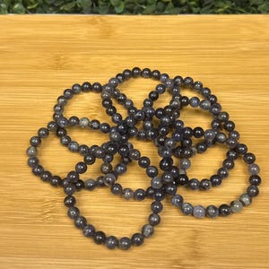 May include: Several dark blue beaded bracelets are arranged on a wooden surface. Each bracelet is made of small, round beads. The bracelets are a mix of dark blue and gray tones, creating a subtle color variation.