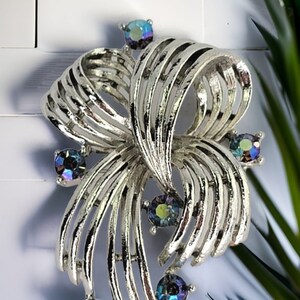 Puede incluir: Un broche de tono plateado con un diseño de cinta en espiral y diamantes de imitación azules iridiscentes.