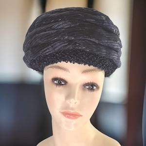 May include: A black, textured, pillbox hat with a beaded trim. The hat is worn on a mannequin's head.