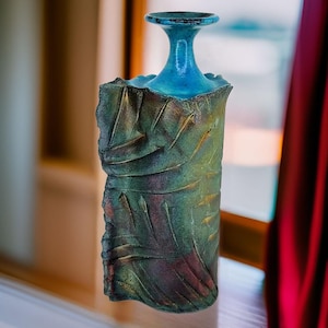 May include: A teal blue ceramic vase with a textured, iridescent surface. The vase has a wide, open mouth and a narrow neck.