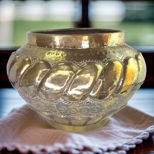 May include: A large, gold-colored brass bowl with a decorative, rope-like design and intricate etched patterns around the rim.
