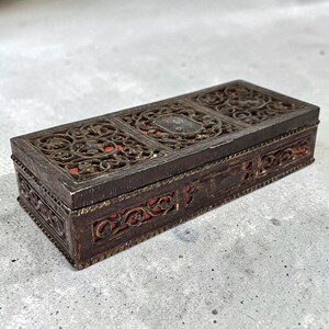 May include: Rectangular antique wooden box with ornate, openwork metal filigree on the lid and sides. The interior is lined with red fabric. The box has a dark brown finish and appears to be aged.