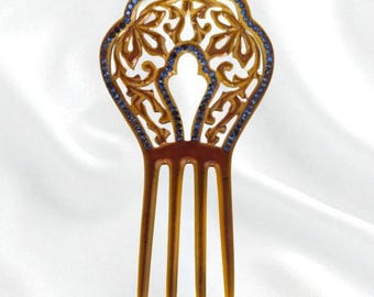 May include: A decorative hair comb with a floral design. The comb is a warm brown color with a decorative top outlined with blue gemstones. The comb has three long, slender teeth.