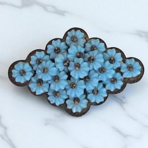 Puede incluir: Broche vintage con cuentas en forma de flor azul claro con centros oscuros. Las flores están dispuestas dentro de un marco marrón oscuro en forma de nube. Accesorio decorativo, probablemente de vidrio.