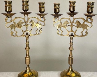 Può includere: Un paio di candelabri antichi in ottone. Ogni portacandele presenta un motivo decorativo a leone e ha quattro portacandele. I candelabri hanno una base rotonda e uno stelo dettagliato. L'ottone ha una calda tonalità dorata.