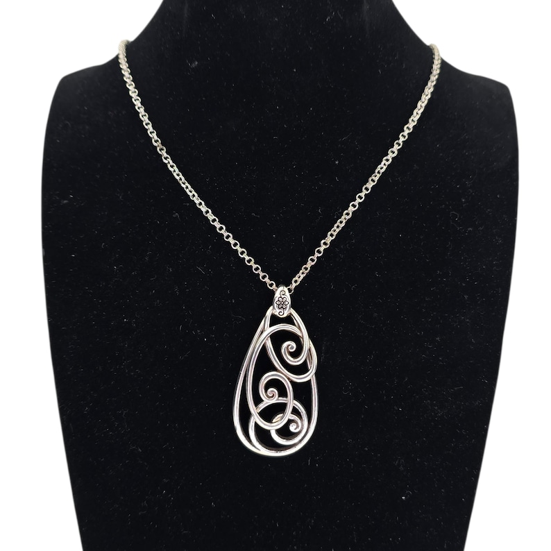 Może przedstawiać: Srebrny naszyjnik z wisiorkiem w kształcie łzy. Wisiorek ma ażurowy wz&oacute;r z wirującymi wzorami. Naszyjnik jest prezentowany na czarnej aksamitnej powierzchni.