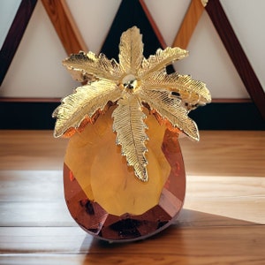 May include: A gold-toned palm tree brooch with a faceted amber-coloured glass base.