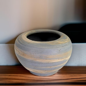 May include: A grey and beige ceramic planter with a wide, round opening. The planter has a swirling pattern of light and dark grey and beige.