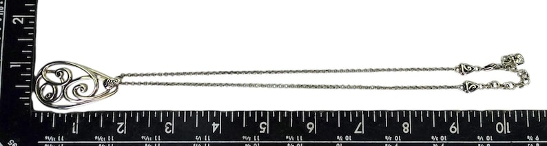 Może przedstawiać: Srebrny naszyjnik z wisiorkiem w kształcie łzy z ażurowym wzorem wirujących wzor&oacute;w. Łańcuszek ma długość około 45 cm, z ozdobnym zapięciem.