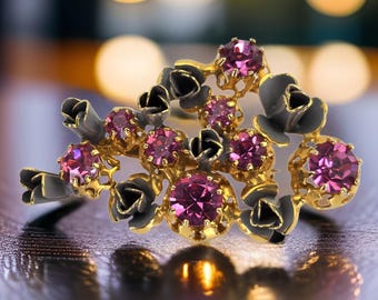 Puede incluir: Un broche de tono dorado con un grupo de diamantes de imitación rosas engastados en un diseño floral. El broche presenta detalles en esmalte negro y un diseño delicado e intrincado.