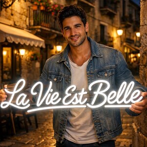 May include: A man holds a white neon sign that reads "La Vie Est Belle". He is wearing a denim jacket, a white t-shirt, and dark blue jeans. The background is a European street scene at night.