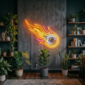 Puede incluir: Un letrero de neón con forma de cometa con luces naranjas, amarillas y rosas cuelga de una pared gris. La habitación está decorada con plantas, estanterías de madera, libros y un escritorio, creando un interior moderno y acogedor.