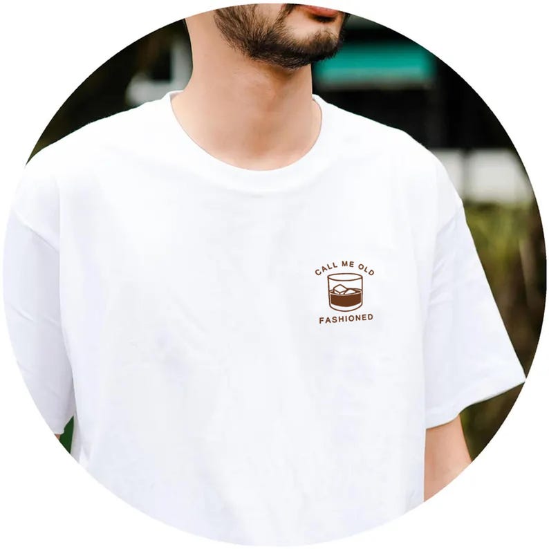 May include: White t-shirt with a brown graphic of a glass of whiskey with ice and the text "Call me old fashioned".