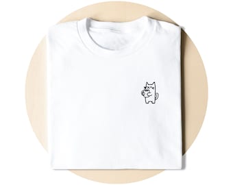 Op de afbeelding: Een wit t-shirt met een kleine, zwarte, minimalistische lijntekening van een kat die een koffiemok vasthoudt op de linkerborst. De kat heeft gesloten ogen en een eenvoudige omtrek, gecentreerd op de witte stof van het shirt.
