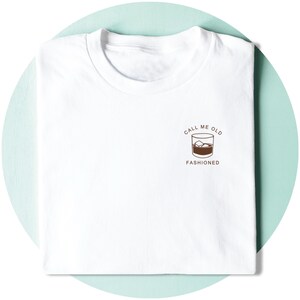 May include: White t-shirt with a brown graphic of a glass of whiskey with ice cubes and the text "Call me old fashioned".
