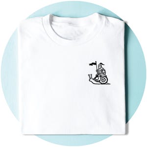 May include: White t-shirt with a black illustration of a knight on a snail, holding a flag. The design is on the upper left chest. The t-shirt is neatly folded, ready to wear.
