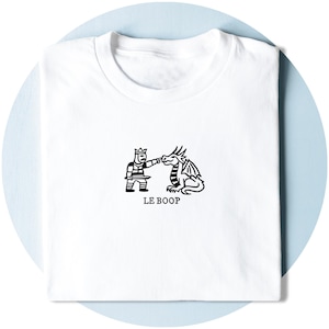 Könnte beinhalten: Ein weißes T-Shirt mit einer schwarzen Strichzeichnung eines Ritters in Rüstung, der einen Drachen an der Nase stupst. Unter der Illustration ist der Text LE BOOP in einer einfachen schwarzen Serifenschrift gedruckt. Das T-Shirt hat einen Rundhalsausschnitt.