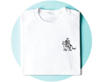 Op de afbeelding: Een wit T-shirt met korte mouwen en een kleine zwarte lijntekening op de borst. De illustratie toont een persoon met een kroon die op de rug van een kat rijdt. Het ontwerp is eenvoudig, strak en bevindt zich aan de rechterkant van het shirt.