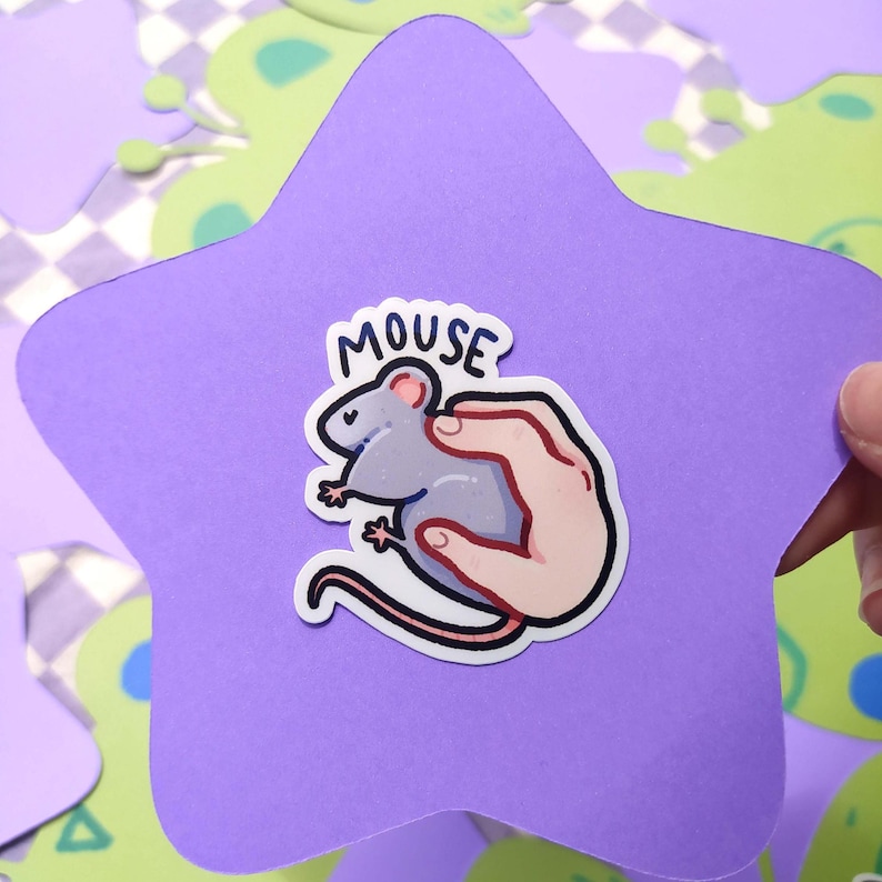 May include: A sticker featuring a cartoon mouse held in a hand, with the word "MOUSE" above. The sticker is on a purple star-shaped cutout, with a light green and purple background.
