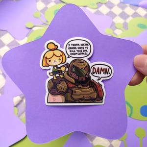May include: A purple star-shaped sticker featuring a cartoon illustration. The sticker depicts a character from Animal Crossing holding a gun, standing on the shoulder of a Doom Slayer character. Text bubbles read "I THINK WE'RE GONNA HAVE TO KILL THIS GUY, DOOMSLAYER" and "DAMN."