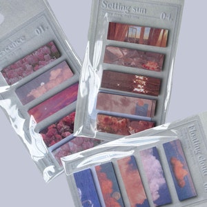 May include: Three packs of decorative sticky notes. Each pack contains several rectangular notes with landscape images. The packs are labelled "Florescence", "Setting sun", and "Floating cloud". The notes feature images of flowers, clouds, and sunsets.