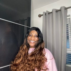 May include: A woman with long, wavy brown and black hair wearing a pink t-shirt.