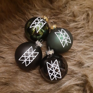 Könnte beinhalten: Vier Weihnachtskugeln mit einem weißen geometrischen Muster auf schwarzem und grünem Hintergrund. Die Kugeln liegen auf einer braunen, flauschigen Oberfläche.