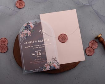 Invitación de boda acrílica con arco floral, sobre rosa palo con detalles en lámina dorada, monograma dorado y opción de sello de cera.