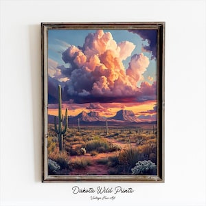 以下が含まれることがあります： 空に大きく劇的な雲の塊が浮かぶ砂漠の風景を描いた絵画。雲はピンク、オレンジ、パープルの色合いで構成されています。砂漠は、いくつかのサボテンや他の砂漠の植物がある、落ち着いた茶色です。絵画は、濃い茶色の額縁に入っています。