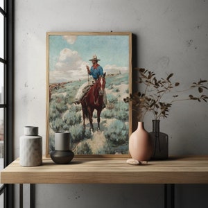 May include: A vintage painting of a cowboy riding a brown horse through a field of sagebrush. The cowboy is wearing a blue shirt, a brown hat, and jeans. The sky is blue with white clouds.