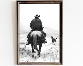 Puede incluir: Fotografía en blanco y negro de un vaquero montando a caballo a través de un paisaje nevado. El vaquero lleva un sombrero y un abrigo largo. Un pequeño perro negro corre delante del caballo.