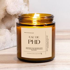 May include: A brown glass candle jar with a white label that reads "Eau de PHD" and "Elevate your senses with the aroma of educational mastery." The candle is lit and the flame is visible.