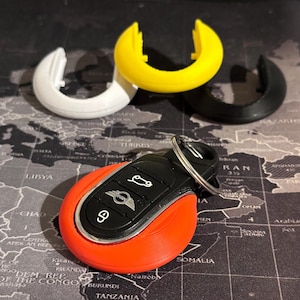 May include: A red, black, and silver car key fob with a MINI logo. The key fob is surrounded by three key fob covers in white, yellow, and black.