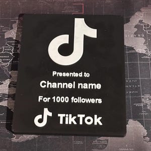 Peut inclure: Plaque noire avec un logo TikTok blanc et le texte "Pr&eacute;sent&eacute; &agrave; Channel name Pour 1000 abonn&eacute;s TikTok".