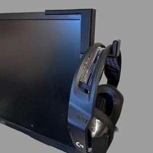 May include: A black computer monitor with the text "G2460P" is shown with a black and silver gaming headset hanging on the side. The headset has the text "G733" and the Logitech logo.