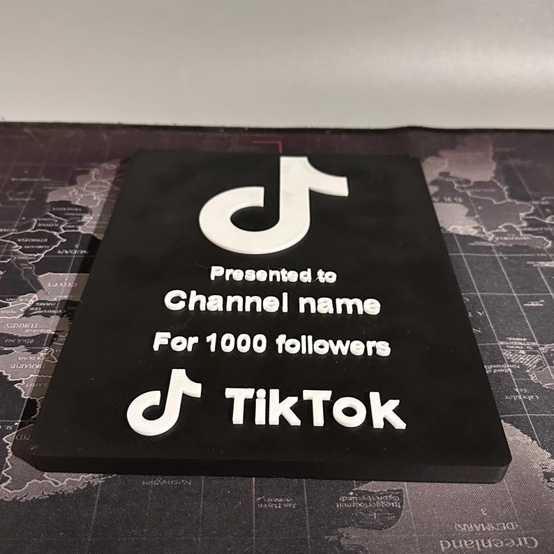 Peut inclure: Une plaque noire avec un logo TikTok blanc et le texte "Pr&eacute;sent&eacute; &agrave; Channel name Pour 1000 abonn&eacute;s TikTok".