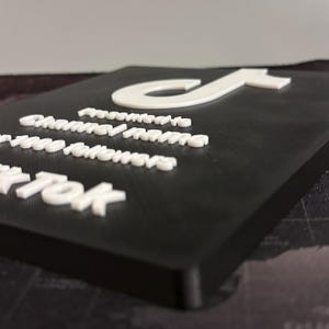 Peut inclure: Une plaque noire avec un logo TikTok blanc et le texte "Promu &agrave;", "Nom de la cha&icirc;ne", "1000 abonn&eacute;s" et "TikTok".