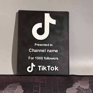 Peut inclure: Plaque noire avec un logo TikTok blanc et le texte "Pr&eacute;sent&eacute; &agrave; Channel name Pour 1000 abonn&eacute;s"