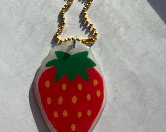 May include: A red and green strawberry keychain with a gold chain. The strawberry is made of plastic and has a glossy finish.