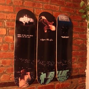 Puede incluir: Tres tablas de skate negras y blancas con dise&ntilde;os diferentes. La primera tabla tiene el texto "When we all fall asleep where do we go?" La segunda tabla tiene el texto "Happier Than Ever". La tercera tabla tiene el texto "Why are things so heavy?" y "Blue Banisters".