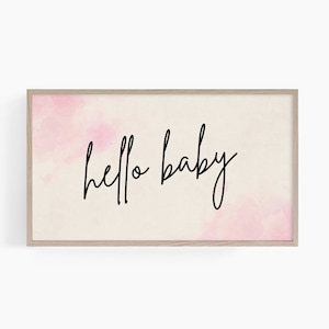 May include: A framed print with a watercolor background in shades of pink and a black cursive inscription that reads "hello baby".