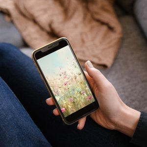 May include: A person is holding a smartphone with a floral wallpaper. The wallpaper features a field of pink and white flowers with a blurred background.