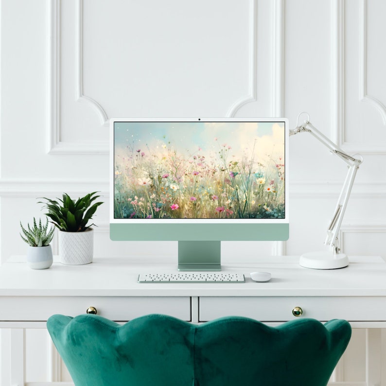 May include: A white desktop computer with a green screen displaying a field of wildflowers. The computer is on a white desk with a white lamp and a keyboard. A green velvet chair is in the foreground.
