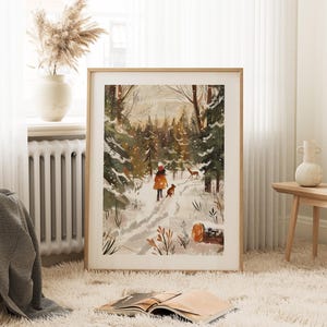 May include: A framed art print depicts a winter scene with a person and a dog walking on a snowy path through a forest. The artwork features a warm color palette with shades of brown, orange, and green. A deer is also visible in the distance.