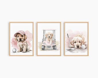 Könnte beinhalten: Set aus drei gerahmten Aquarelldrucken mit Golden Retriever-Welpen. Ein Welpe trägt eine rosa Kappe und sitzt in der Nähe eines Golfballs. Ein anderer sitzt in einem rosa Golfwagen. Der dritte liegt in der Nähe eines Golfschlägers und -balls.